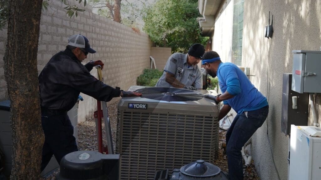 three people putting down furnace behind a house